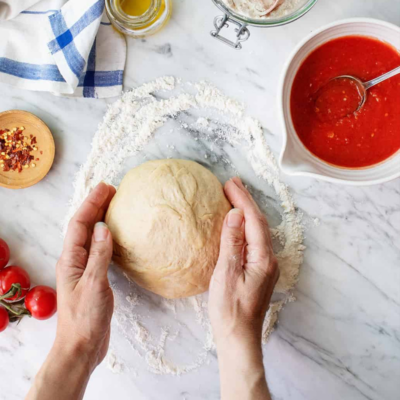 Masa de pizza junto a tomate y salsa